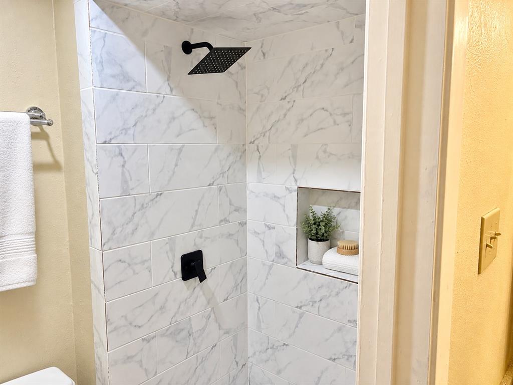 Shower enclosure featuring large-format veined tile, matte black rainfall showerhead, matching single-handle valve, and a built-in recessed storage niche