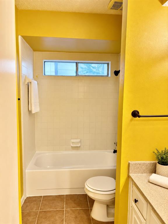 Bathroom featuring a tub-shower combination with ceramic tile surround, integrated soap dish, horizontal slider window, and stone-finish vanity countertop
