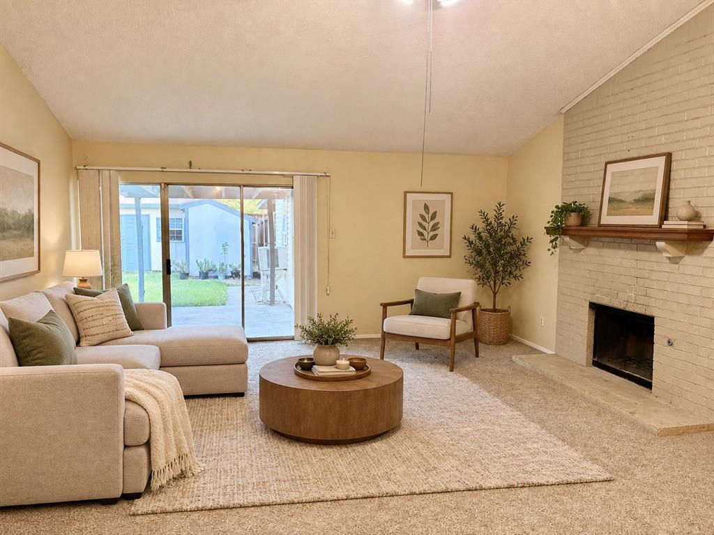 Vaulted ceiling, floor-to-ceiling brick fireplace with a wood mantel, and glass sliding door opening to a concrete patio