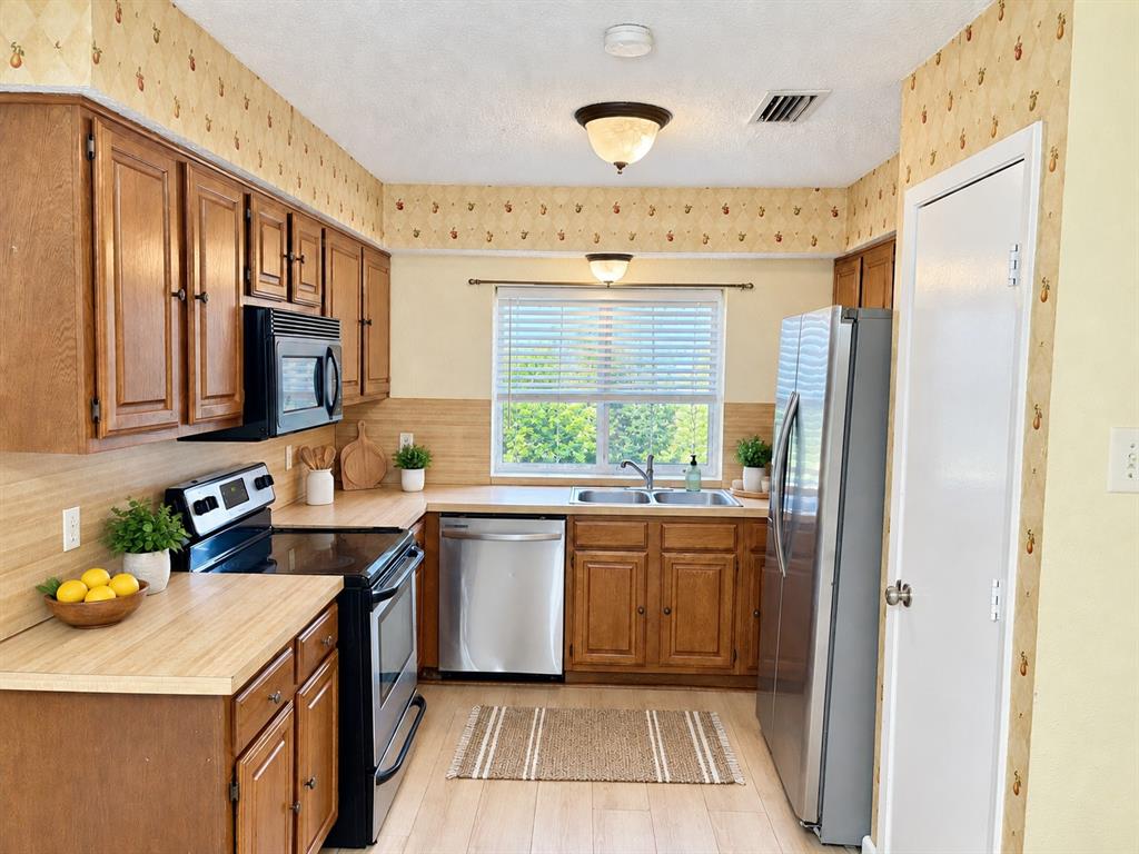 Kitchen featuring wood cabinetry, stainless steel appliances, dual-basin sink, laminate countertops, and wood-finish flooring