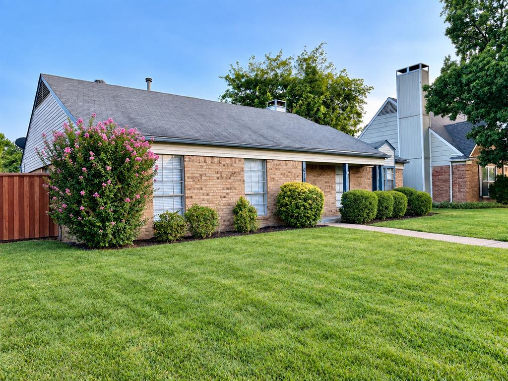 Brick exterior featuring a multi-gabled roofline, prominent chimney, wood-tone fencing, and manicured landscaping