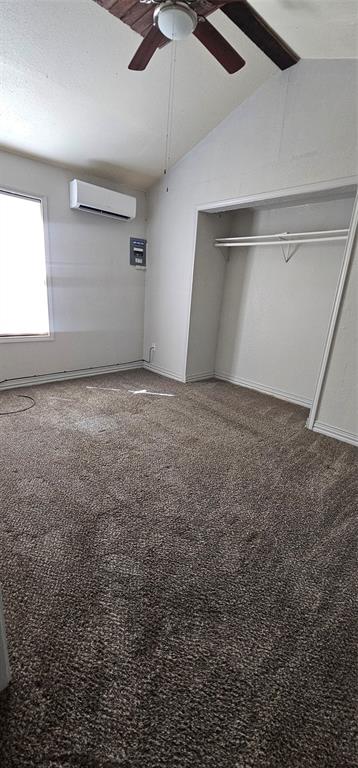 Vaulted ceiling with a ceiling fan, wall-mounted climate control unit, closet with integrated shelving, and neutral wall-to-wall carpeting