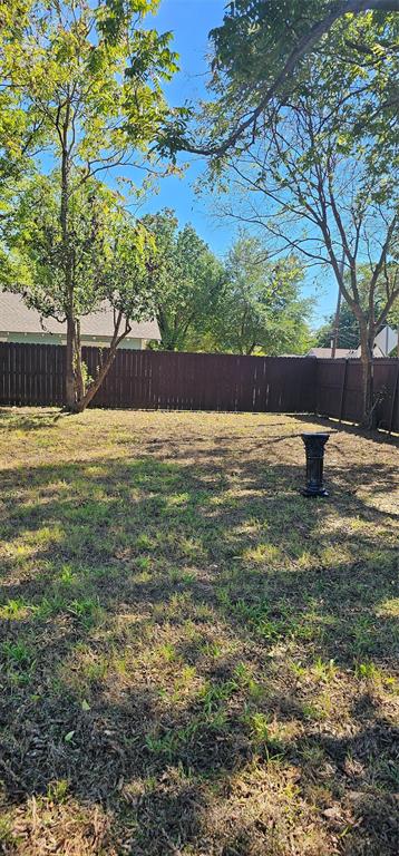 Expansive backyard featuring a solid-panel privacy fence and mature trees