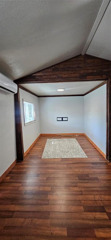 Interior space featuring vaulted ceilings, dark wood-tone trim accents, wood-finish flooring, and a wall-mounted ductless mini-split HVAC unit