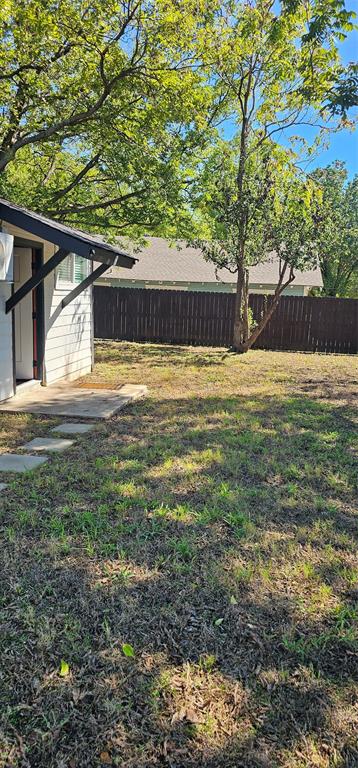 Exterior backyard featuring a concrete patio, stone paver walkway, mature trees, and a wood privacy fence