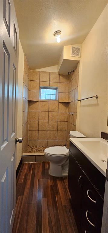 Bathroom featuring a walk-in shower with tile surround and stone flooring, wood-finish flooring, dark cabinetry with a white countertop, and a recessed window