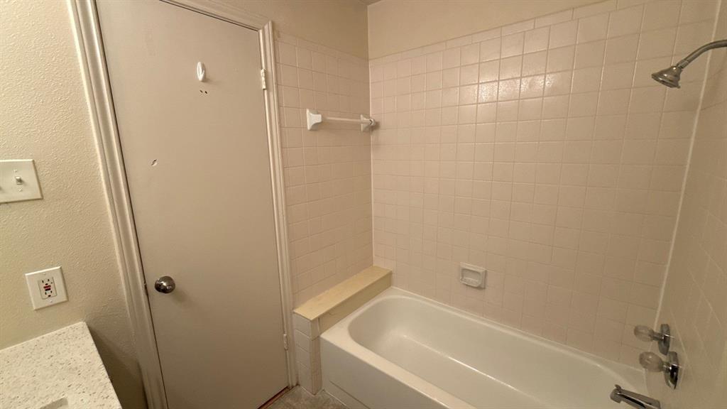Bathtub featuring white square tile surround, integrated tiled ledge, and chrome-finish fixtures