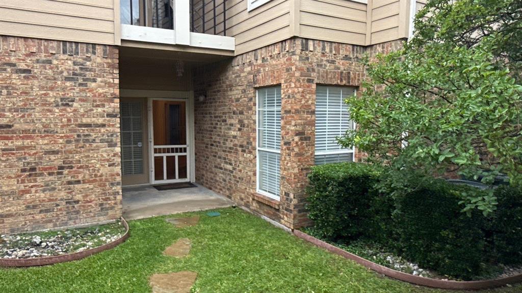 Brick exterior facade featuring horizontal siding accents, a recessed entryway, multi-paned windows, and manicured landscaping with stone-bordered garden beds