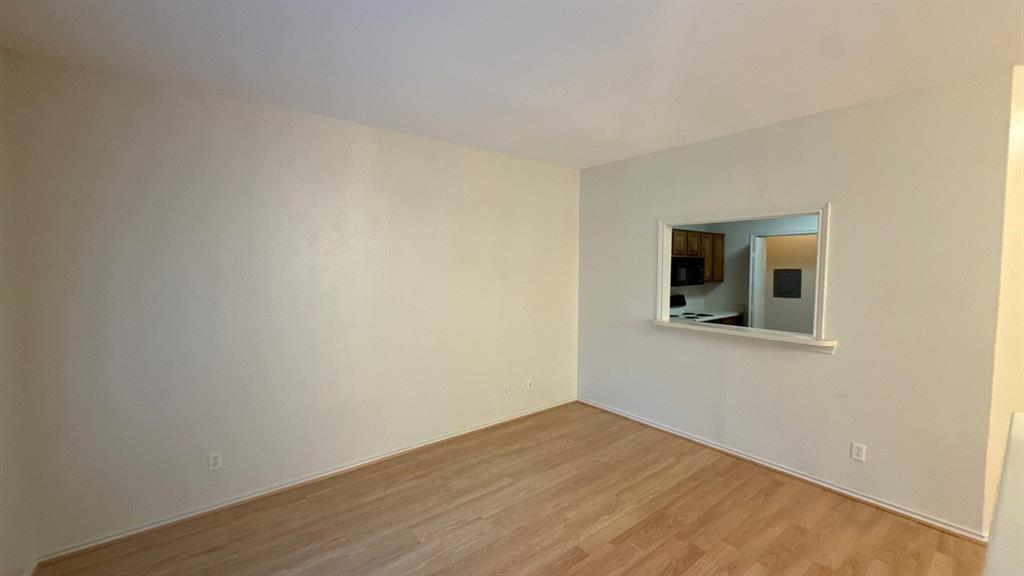 Neutral-toned interior space featuring wood-finish flooring and a rectangular pass-through window with a trim surround