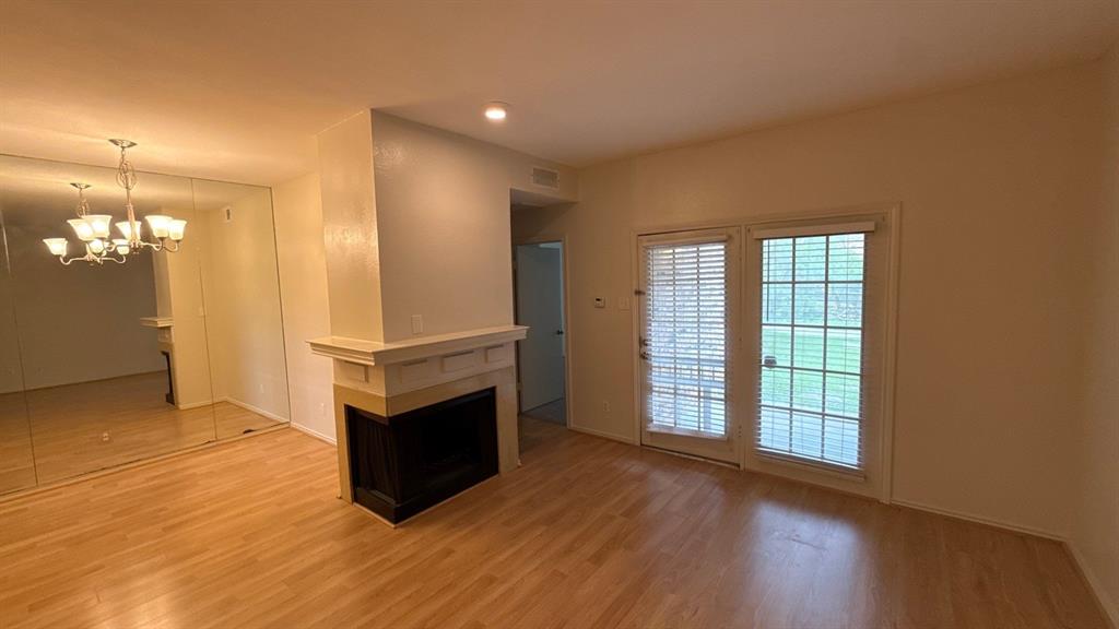 Living area featuring wood-finish flooring, a corner fireplace with a traditional mantel, floor-to-ceiling wall mirrors, and dual glass-paneled doors with integrated window blinds Living area featuring wood-finish flooring, a corner fireplace with a traditional mantel, floor-to-ceiling wall mirrors, and dual glass-paneled doors with integrated window blinds