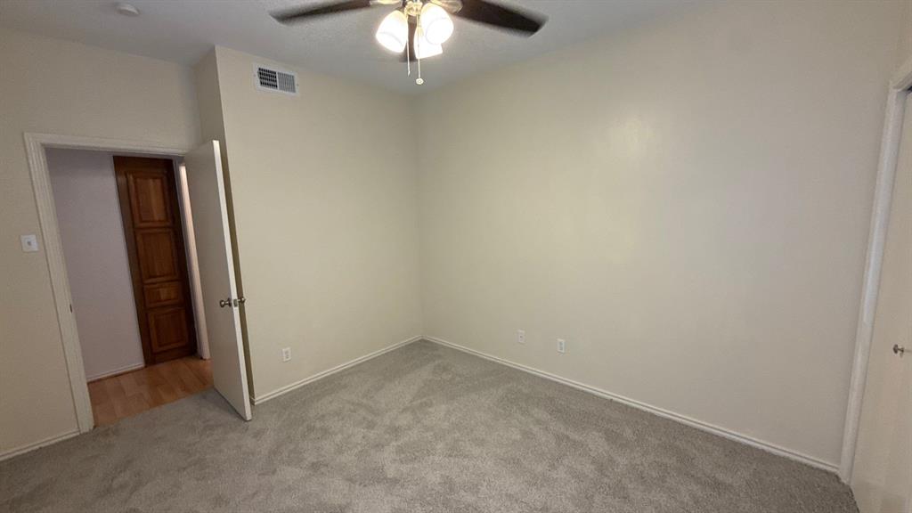 Neutral-toned room with plush carpeting, ceiling fan with light fixture, and wooden paneled door