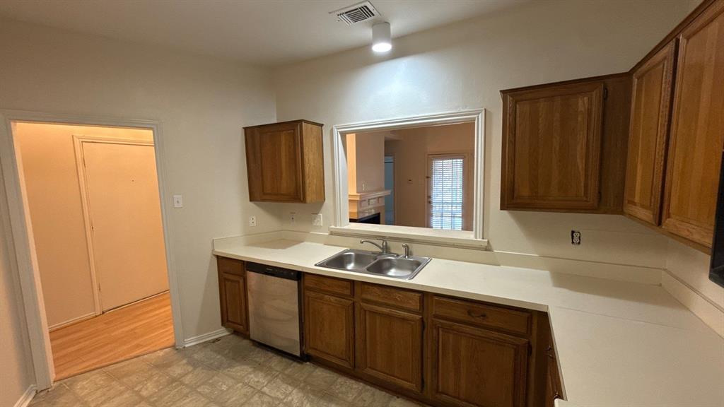 Kitchen featuring wood cabinetry, solid-surface countertops, dual-basin stainless steel sink, and stainless steel dishwasher