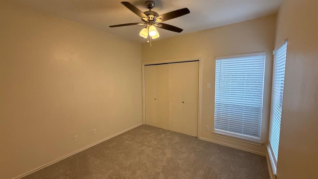 Room featuring neutral wall tones, wall-to-wall carpeting, a ceiling fan with integrated lighting, dual windows with horizontal blinds, and a built-in closet with folding doors