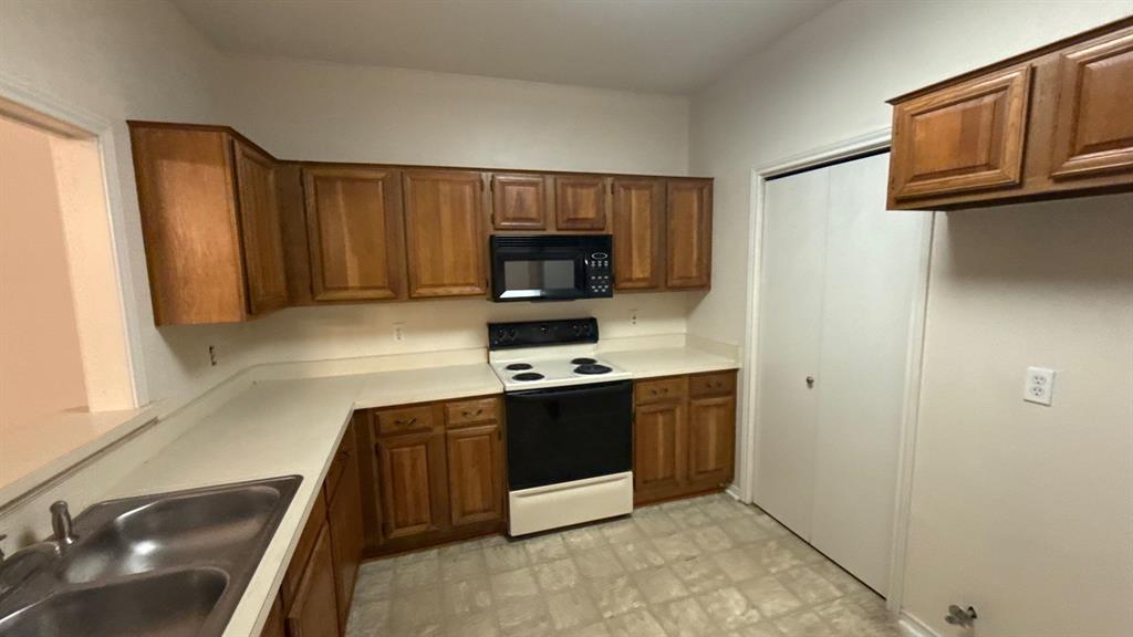 Kitchen featuring wood cabinetry, solid-surface countertops, dual-basin stainless steel sink, over-the-range microwave, and pantry closet