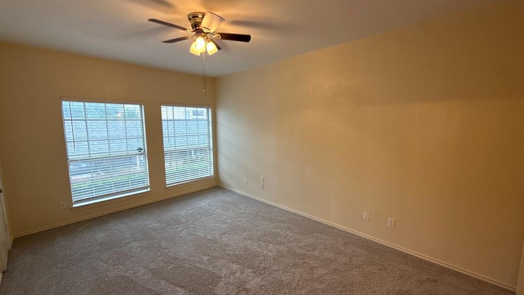 Neutral-toned interior space featuring wall-to-wall carpeting, two dual-pane windows with grid detailing, and a ceiling-mounted light fixture with a fan