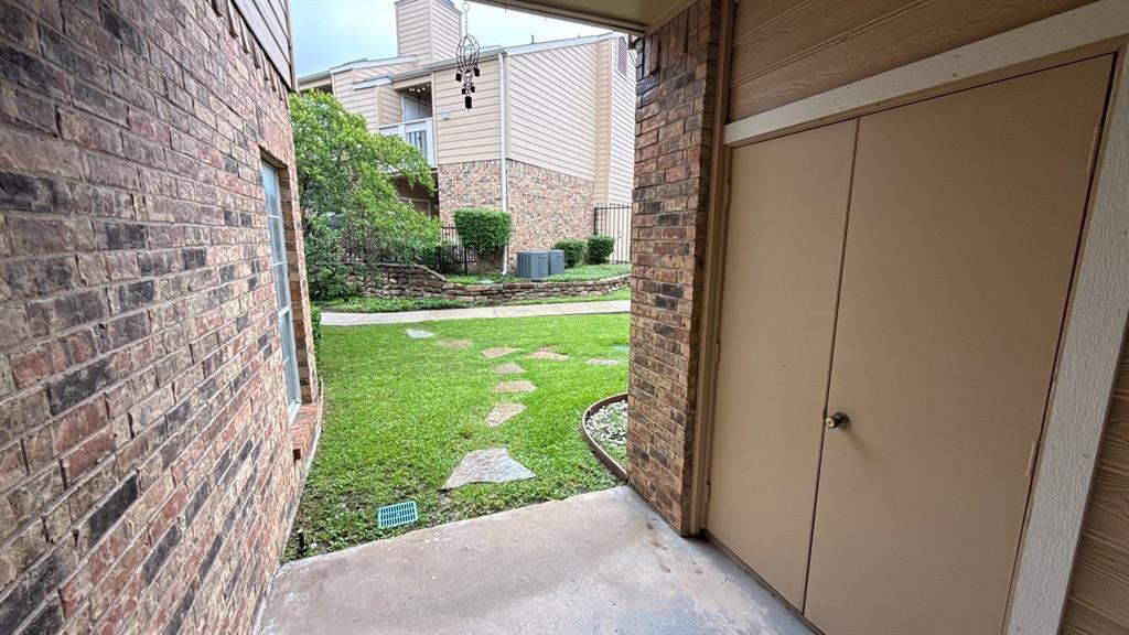 Exterior patio featuring brick masonry, a built-in storage closet with double doors, and a concrete floor surfacing onto a lawn with a natural stone pathway