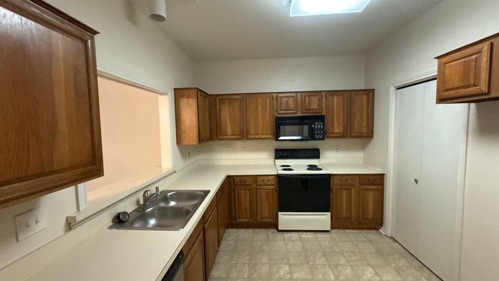 Kitchen featuring natural wood cabinetry, solid surface countertops, dual-basin stainless steel sink, over-the-range microwave, and electric range