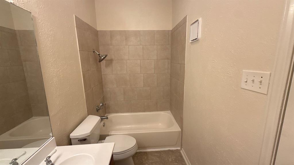 Bathroom featuring a tub and shower combination with neutral tile surround, a built-in vanity with a solid-surface countertop, and a wall-mounted mirror