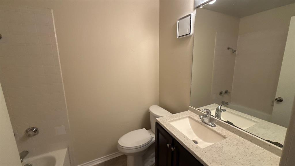 Bathroom featuring a vanity with a light-toned speckled countertop, an integrated basin, a large wall-mounted mirror, and a tub-shower combination with tile surround