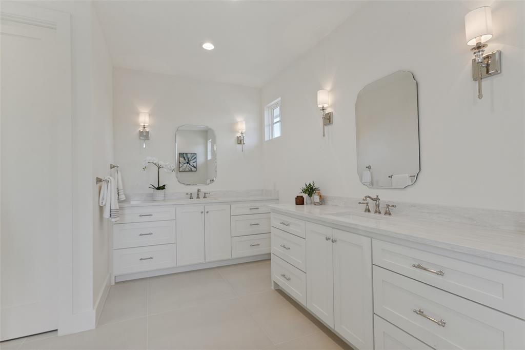 Dual white cabinetry with stone countertops, undermount sinks, polished metal fixtures, and arched wall-mounted mirrors