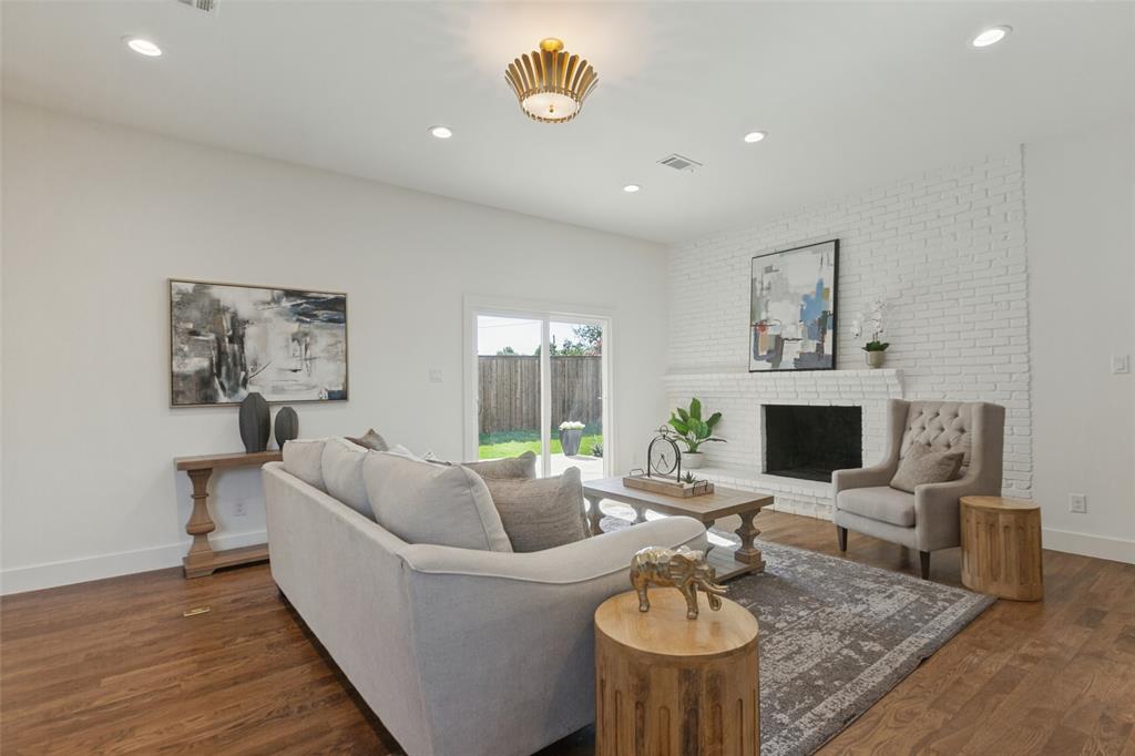 Living area featuring wood-finish flooring, white-painted brick fireplace, recessed lighting, decorative flush-mount fixture, and sliding glass doors