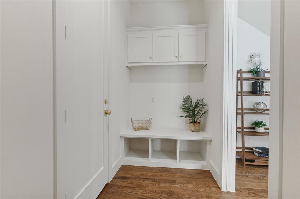 Built-in white cabinetry featuring upper storage units and lower open cubbies with a bench seat, complemented by wood-finish flooring