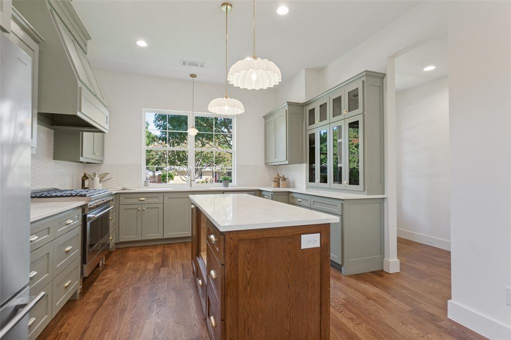 Kitchen featuring sage cabinetry, a wood-finish island with quartz countertops, custom glass-front display cabinetry, wood-finish flooring, and pendant lighting