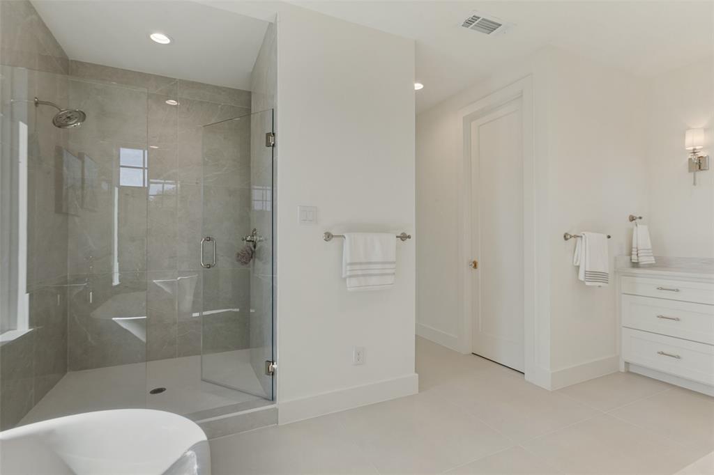 Walk-in shower with floor-to-ceiling tile, frameless glass enclosure, wall-mounted shower head, white vanity with stone countertop, and recessed lighting