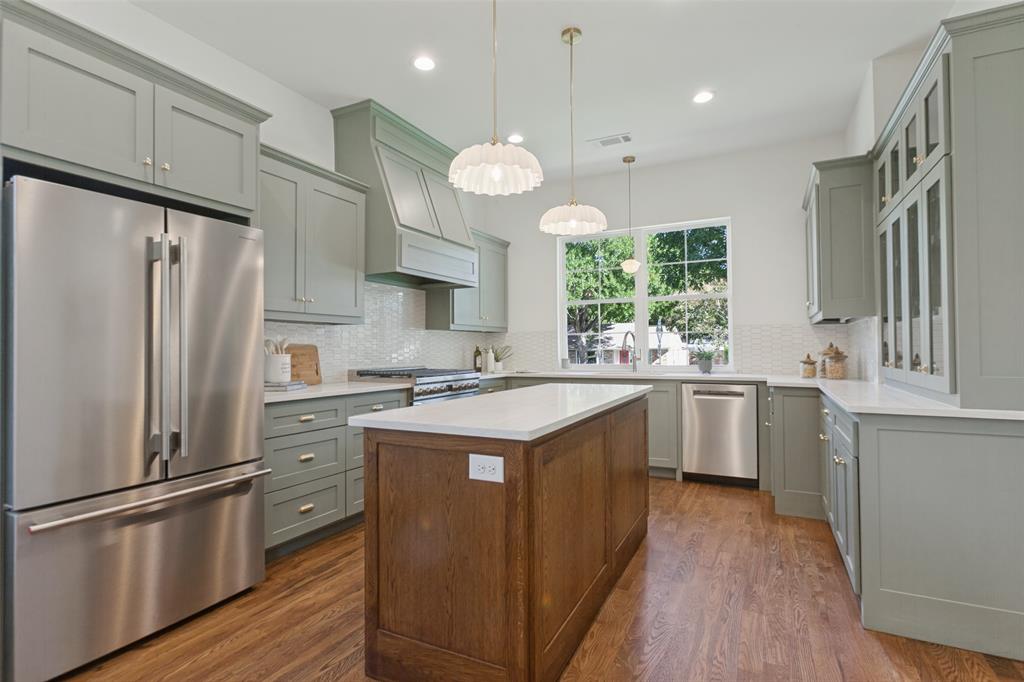 Kitchen featuring sage green cabinetry, a center island with a wood finish, light-toned stone-style countertops, stainless steel appliances, and textured tile backsplash