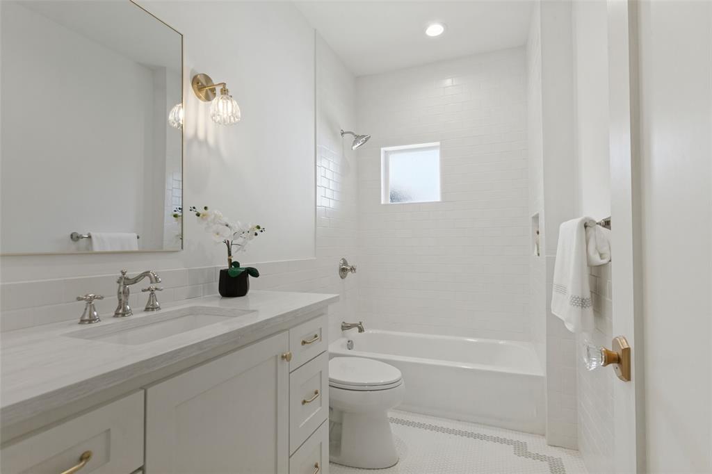 Bathroom featuring white cabinetry, stone-finish countertop, polished metal fixtures, white subway tile shower surround, and mosaic tile flooring