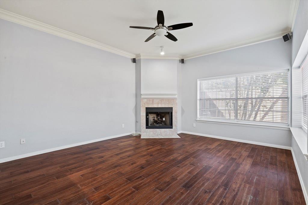 Living area featuring wood-finish flooring, a corner fireplace with stone-surround tile, crown molding, a multi-blade ceiling fan, and large windows with integrated blinds