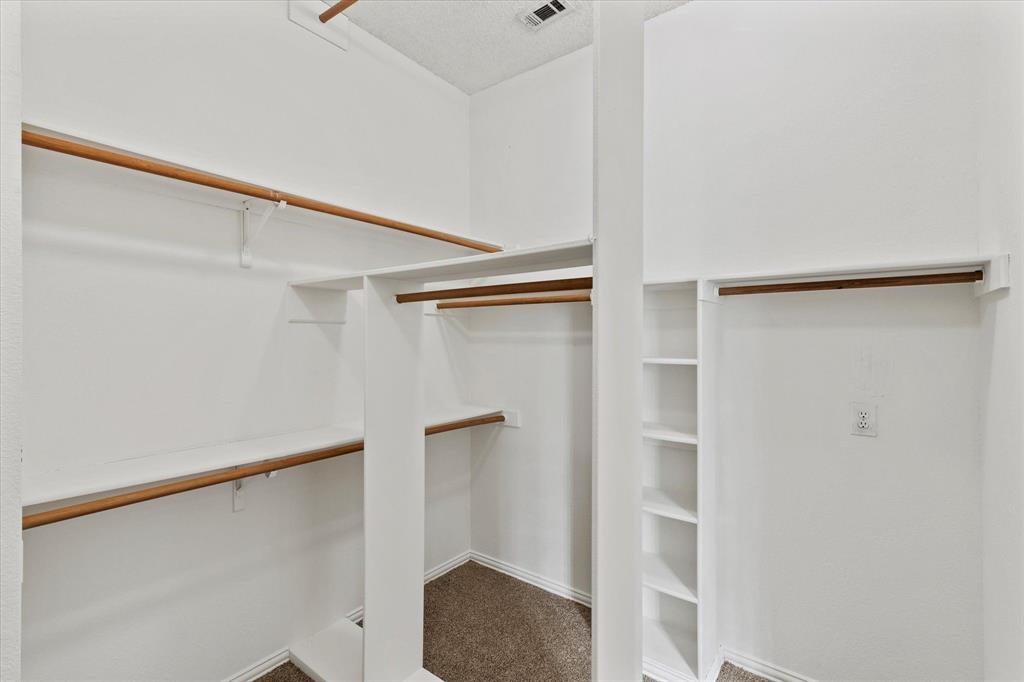 Walk-in closet featuring multi-level hanging rods, built-in shelving units, and neutral carpeting