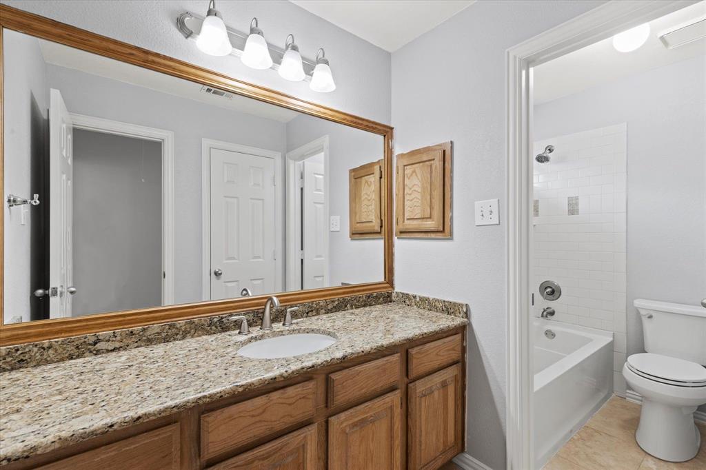 Upstairs 2nd Bathroom featuring a stone-look countertop, wood cabinetry, expansive wall-mounted mirror, four-light vanity fixture, and a tub-shower combination with white subway tile surround