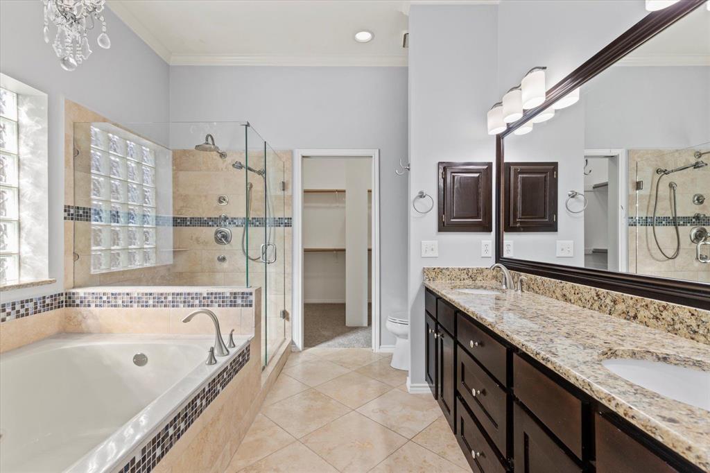 Bathroom featuring a dual-sink vanity with stone countertops, a deep soaking tub, and a separate glass-enclosed shower with tiled surround