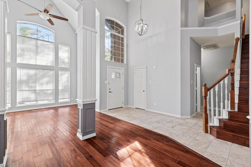 Double-height ceilings featuring large arched windows, wood-finish flooring, tile flooring, and a staircase with a wooden handrail and balusters