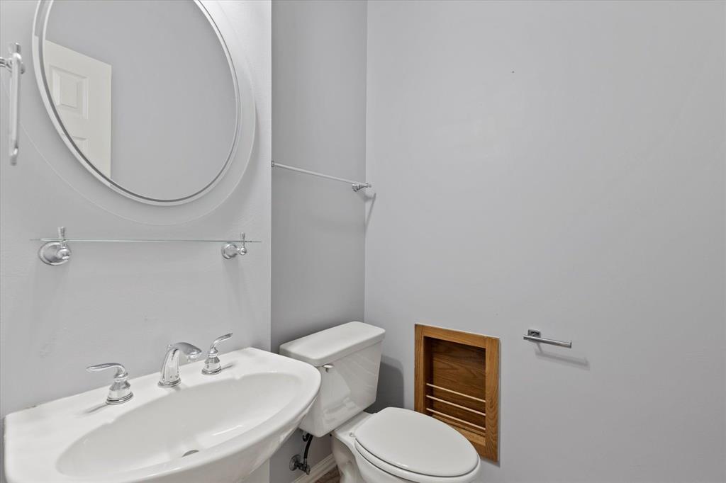 Guest half-bath with Pedestal sink with chrome widespread faucet, oval wall-mounted mirror, glass shelving, and recessed wood-trim wall niche