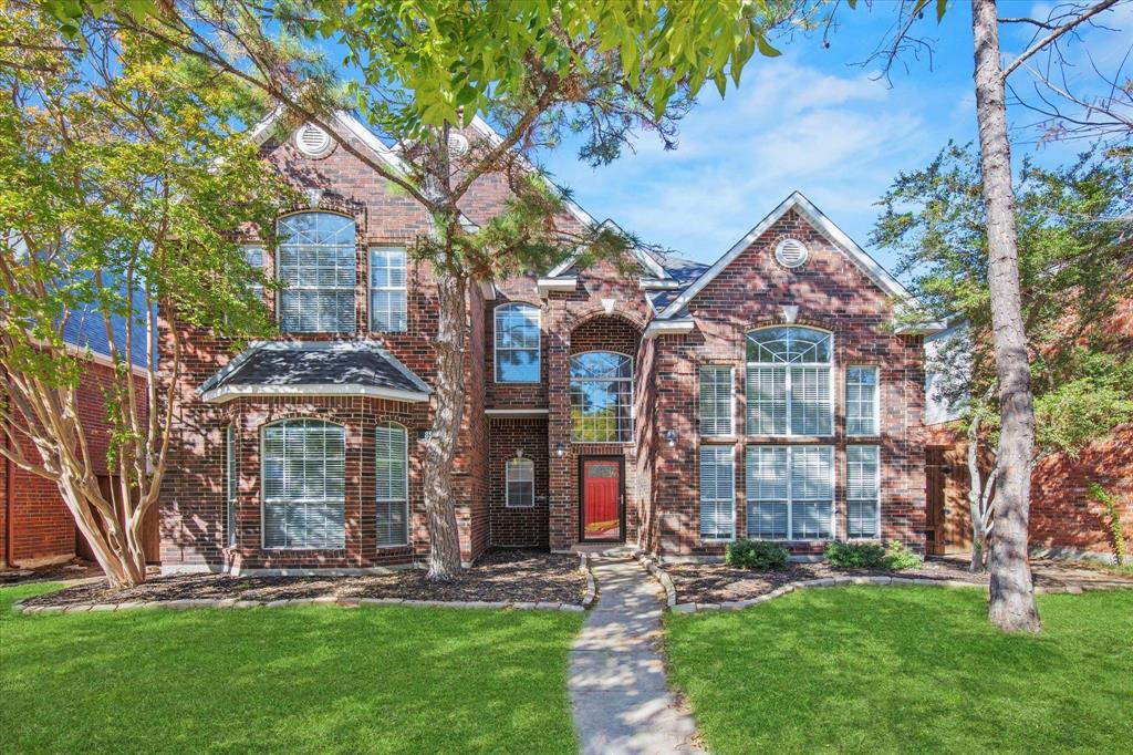 Multi-story brick exterior featuring an arched entryway, gabled rooflines, stone-accented window trim, and large multi-pane windows