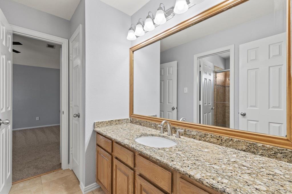 Upstairs Jack and Jill bathroom. Vanity featuring wood cabinetry, stone-finish countertop, undermount sink, expansive wood-framed mirror, and multi-bulb wall-mounted lighting fixture