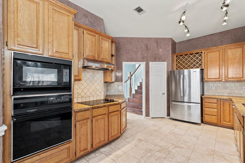 Kitchen featuring custom wood cabinetry, stainless steel appliances, built-in wine storage, tile flooring, and stone-finish countertops