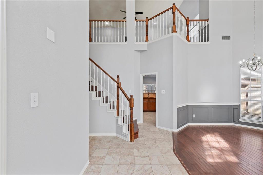 Double-height foyer featuring a staircase with wooden handrails and balusters, tile flooring, wood-finish flooring, and wainscoting