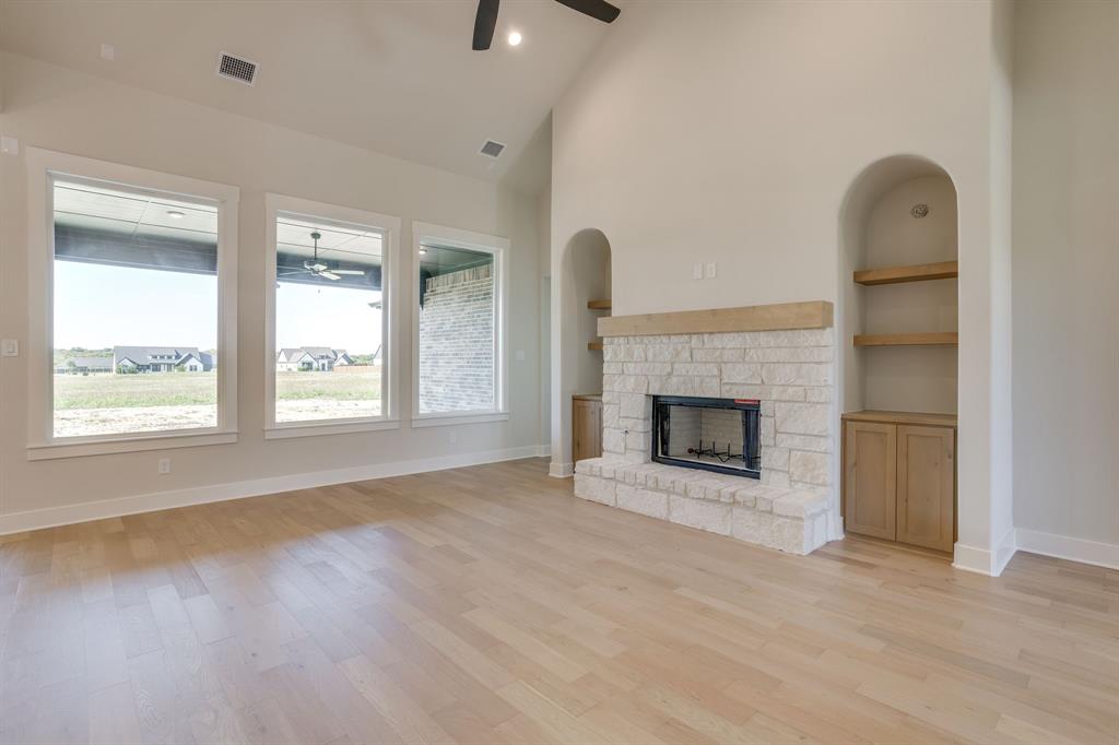 Vaulted ceiling, stone-surround fireplace with a timber mantel, built-in cabinetry, and wood-finish flooring