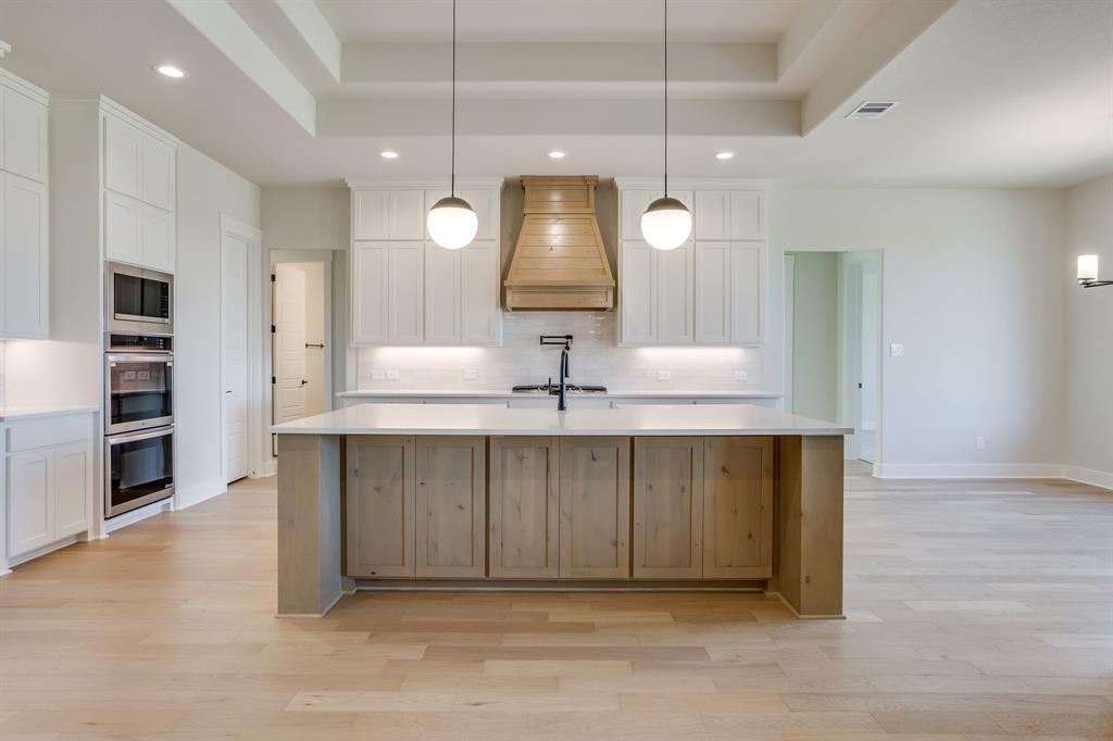 Kitchen featuring white shaker cabinetry, wood-finish center island, quartz countertops, custom wood range hood, and double wall ovens