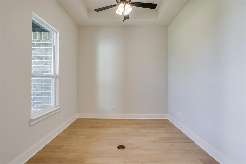 Tray ceiling featuring a central ceiling fan with multi-light fixture, wood-finish flooring, and a single-pane window