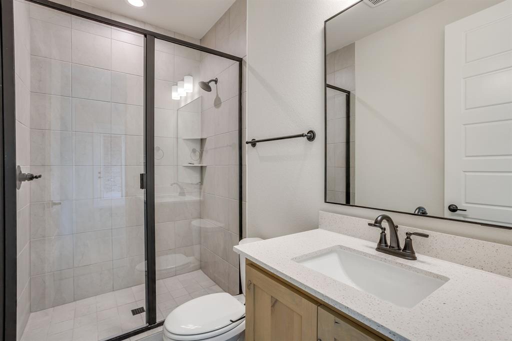 Bathroom featuring a walk-in shower with tile surround, glass enclosure, and matte black fixtures, stone-finish countertop with an undermount sink, and a black-framed mirror