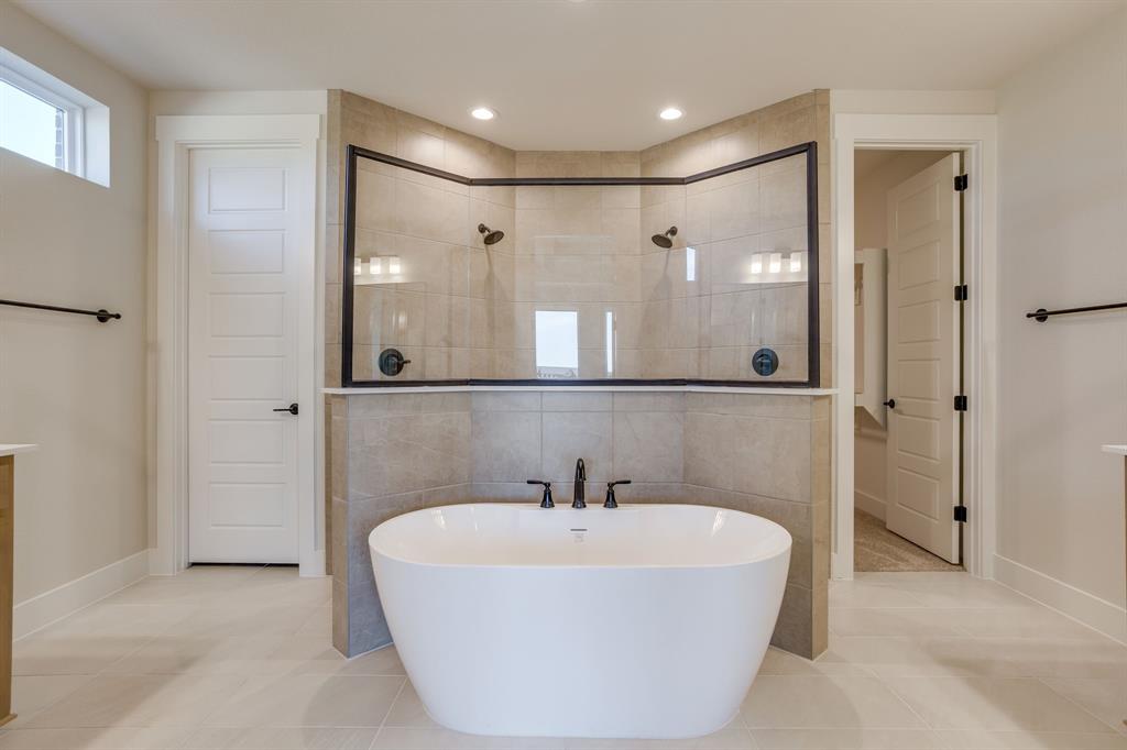 Freestanding soaking tub with a deck-mounted faucet, complemented by an enclosed tile shower featuring dual showerheads, dark metal framing, and a tiled partition wall