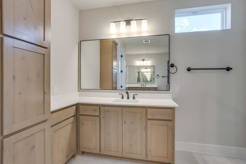 Natural wood-finish cabinetry, quartz countertop with an integrated rectangular sink, large rectangular mirror, matte black fixtures, and transom window