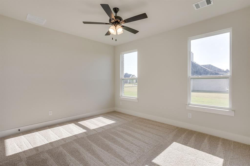 Neutral wall palette with carpeted flooring, dual windows, and a ceiling-mounted light fixture with a fan