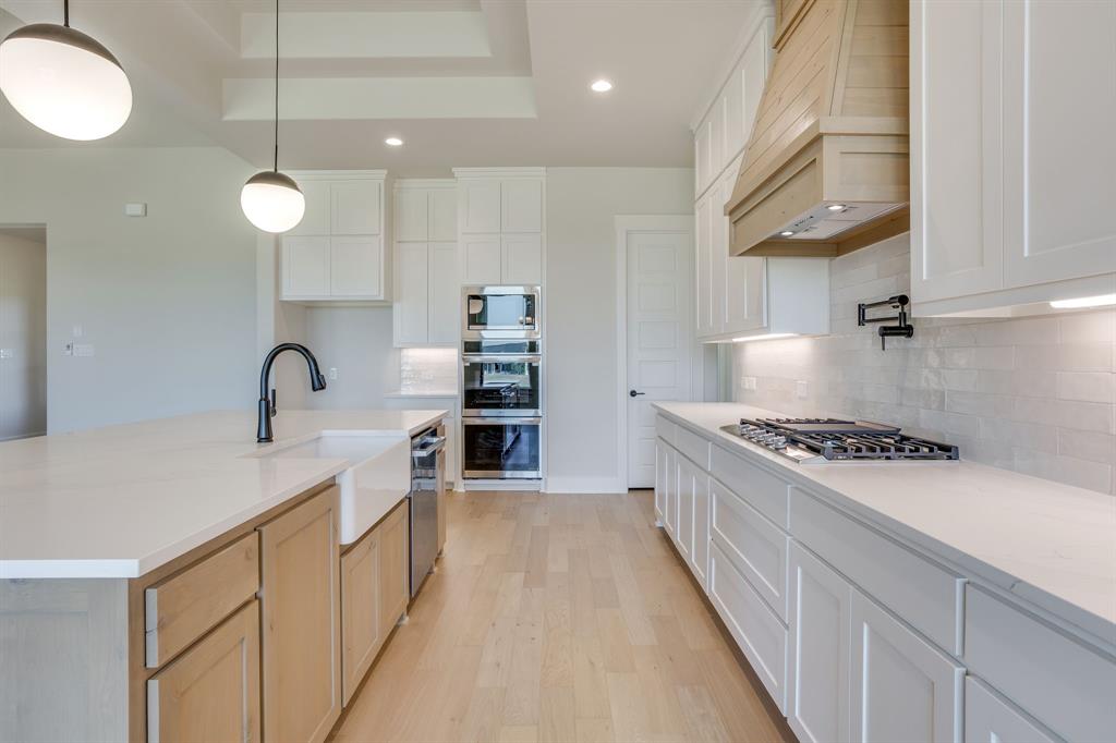 Kitchen featuring white cabinetry, wood-finish island base, quartz countertops, farmhouse sink with matte black faucet, and built-in stainless steel double ovens