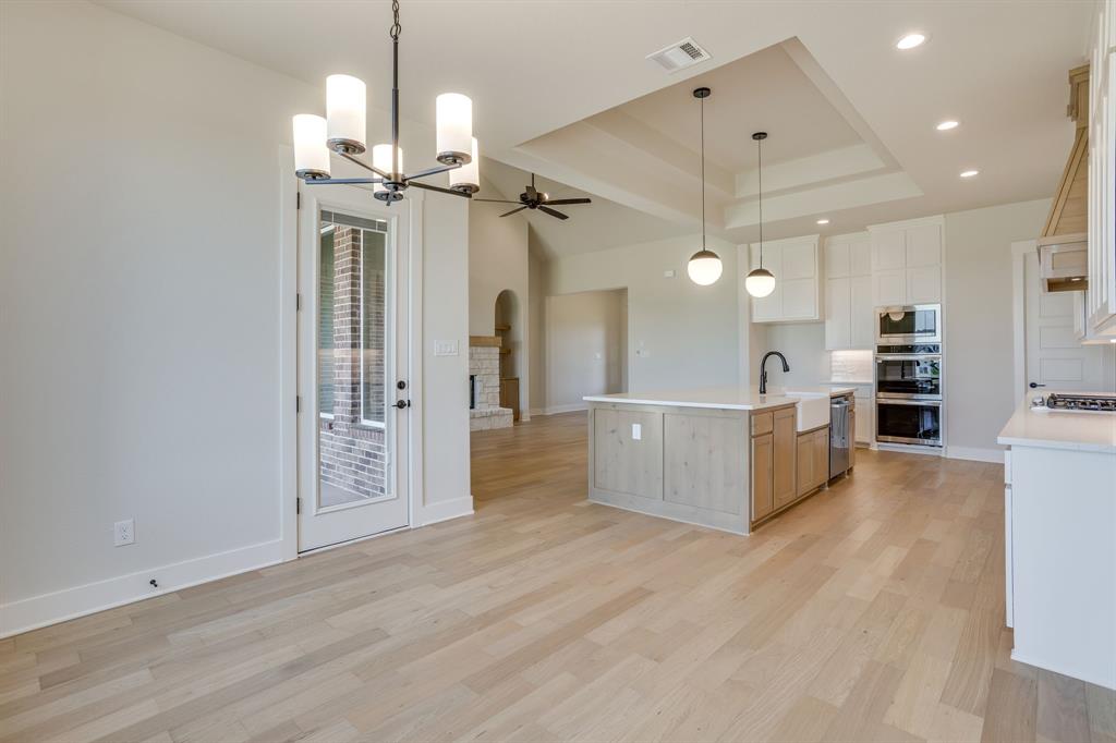 Open-concept kitchen featuring an island with a farmhouse sink, stone countertops, custom cabinetry, stainless steel double wall ovens, and wood-finish flooring