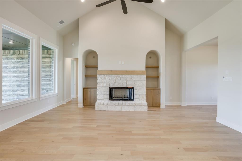 Vaulted ceilings featuring a central fan, light wood-finish flooring, and a floor-to-ceiling stone fireplace surround with a timber mantel